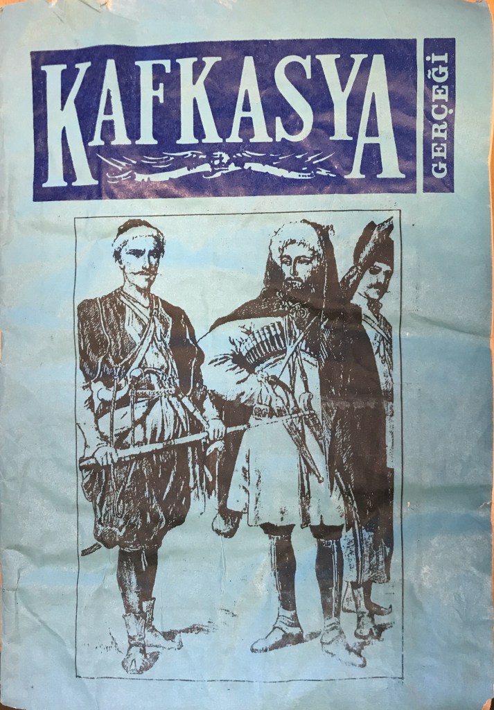 A blue sheet of paper that is water stained and crumpled featuring a black ink drawing of three standing men in traditional North Caucasian dress, each one with weapons, beneath the magazine header of text cut out of a dark blue background. 