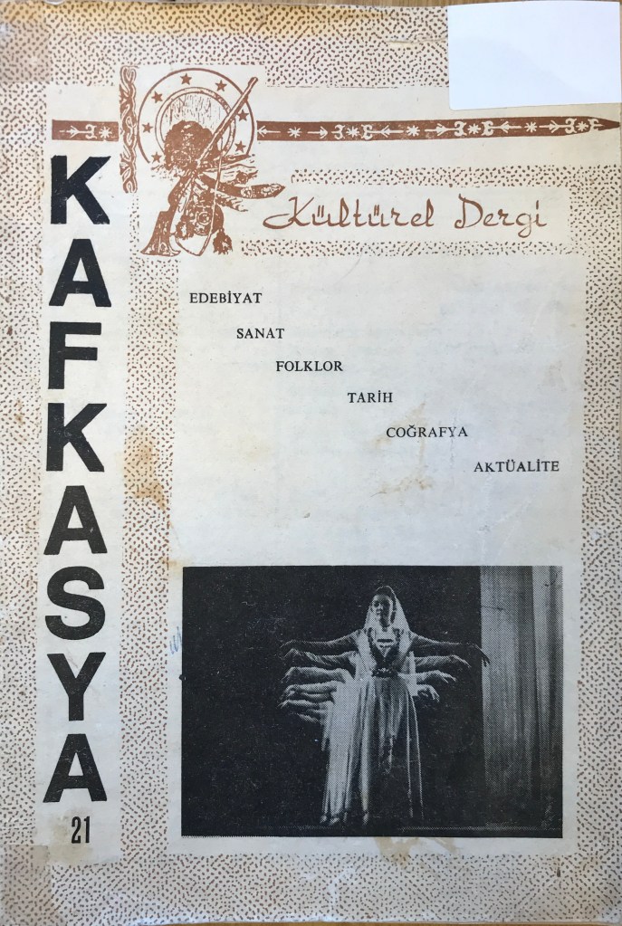 Magazine cover with Latin-script text in black and white, above a black and white photograph of women in traditional North Caucasian dress dancing on stage. The page has a dark orange pattern surrounding the text, and a cursive title in the same coloured ink. 