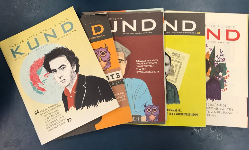 An array of multicoloured magazines splayed over a dark green table. 