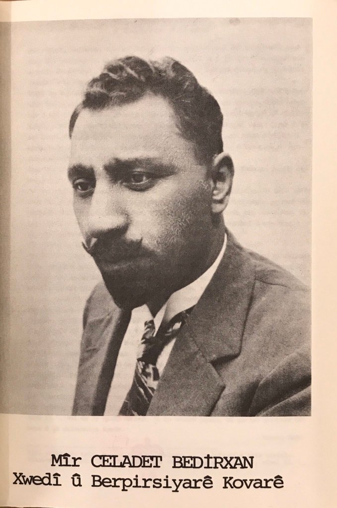 A black and white picture of a man in a suit, chest up, with a tie and a white shirt. The man is looking at the bottom-left corner and has a mustache and goatee.