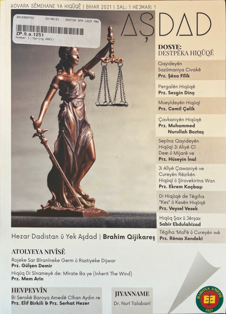 The cover of a magazine in white, off-white and light brown, with black Latin-script text at the top and on the side, with a photograph of Lady Justice as a small statue.