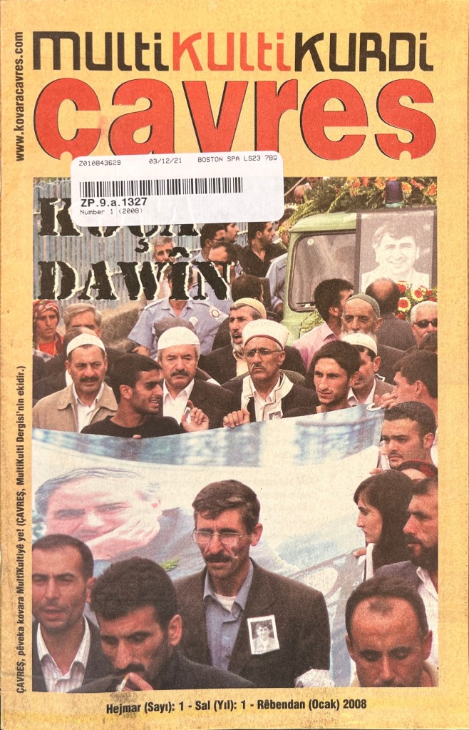 A yellow cover of a magazine with Latin-script text in red and black at the top, above a colour photograph showing a crowd, largely a group of elderly men, marching in a street with a large photograph of a man