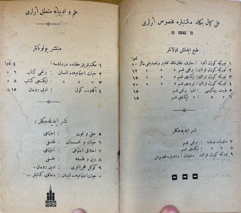 Double-page spread of white paper with black inked text in Arabic script. At the bottom of the right-hand page are three black squares with white oblongs cut out. At the bottom of the left-hand page are three stylized towers, the outer ones with circles atop them and the middle with a tear drop outline. Below them is a white mustache on a black background.
