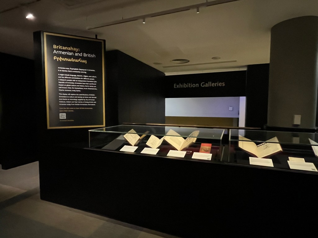 A darkened room with a black panel on a wall featuring white text to the left of two glass cases with books in them