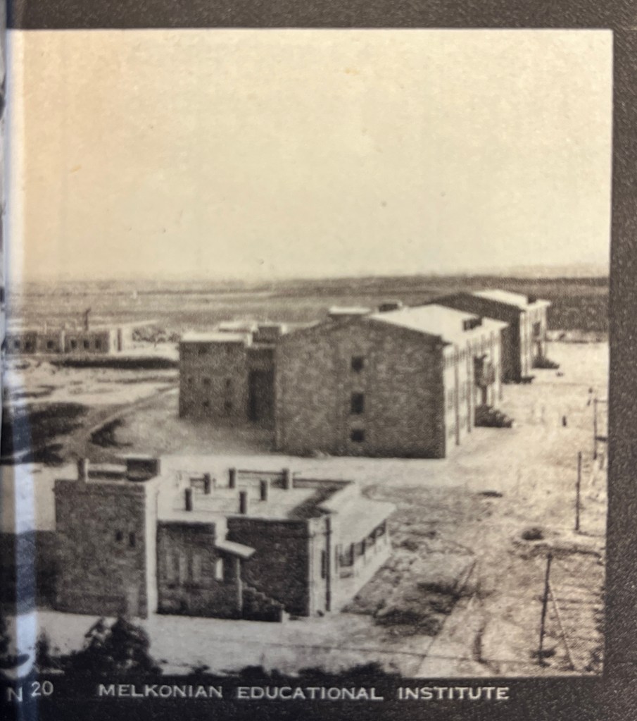 A black and white photo of a three 20th century buildings from the air, a smaller one in the foreground, a large three-storey one in the mid-ground and a small bungalow in the left background. 
