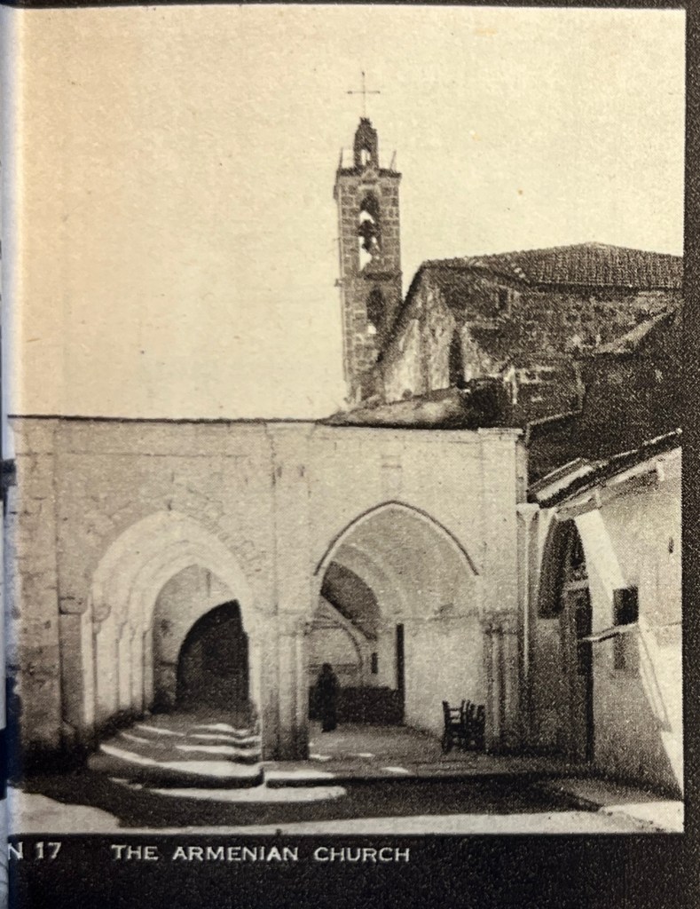 A black and white photograph of the Surp Astvadzadzin Church showing white porticoes in the foreground and the Medieval dark stone structure to their back right. In the background is a belfry in dark stone. 